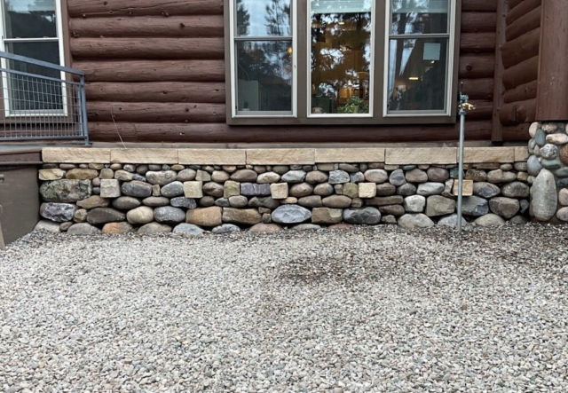 Locally gathered river stone used to construct tradtional double face dry stone retaining wall with flat cap. Through stones in contrasting stone. Solid stone wall.