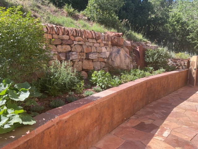 Traditional dry stone retaining wall with vertical copes. Stained concrete wall with mortared natural stone cap. dry laid flagstone, custom metal fence with freestanding stone walls