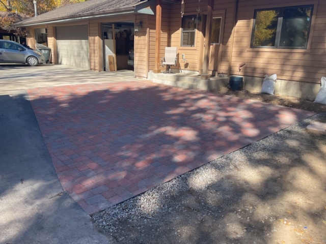 Paver patio installed to driveway specifications. natural sandstone slab stair visible connecting to concrete porch
