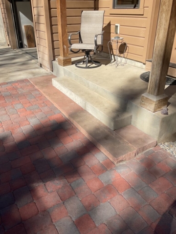 Paver patio installed to driveway specifications. natural sandstone slab stair visible connecting to concrete porch
