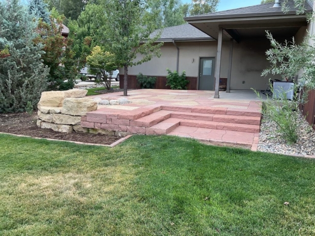Custom-designed terraced flagstone patio with two custom slab sandstone staircases, boulder seating area, and rustic fire pit