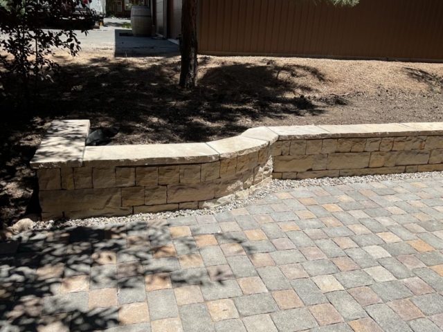 Dry laid paver patio with traditional dry stone retaining wall with mortared cap used as raised bed planter