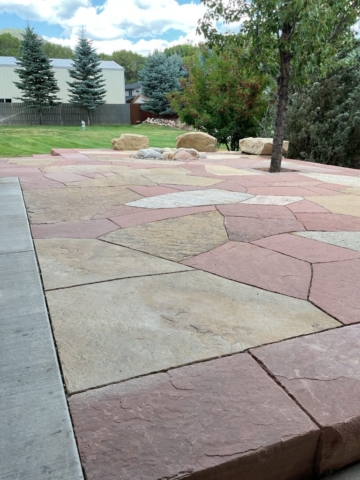 two tone flagstone patio with boulder seating and rustic stone firepit visible.