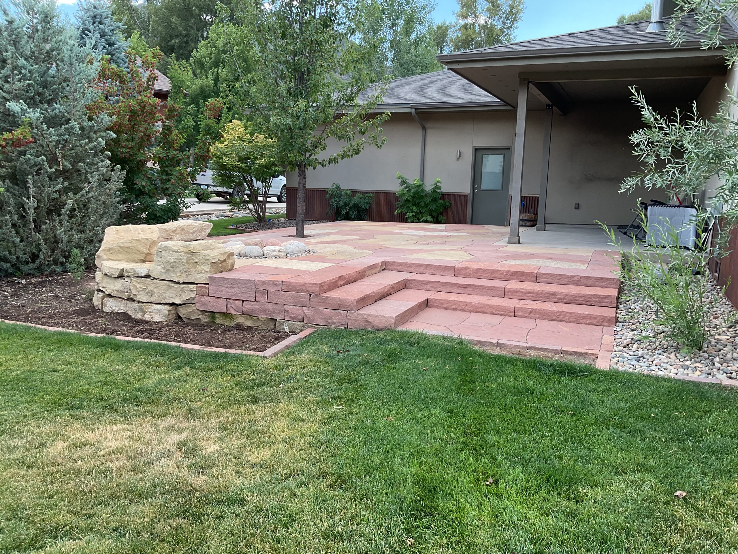 Custom designed flagstone patio terrace with two custom natural stone slab staircases, integrated boulder seating, and rustic fire pit